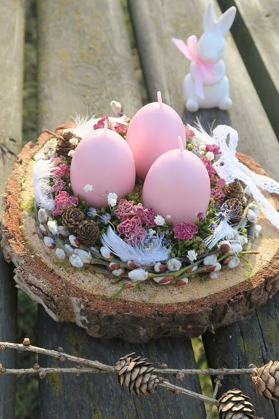 an Easter centerpiece of a tree slice, willow, dried blooms and feathers and pink egg-shaped candles is wow