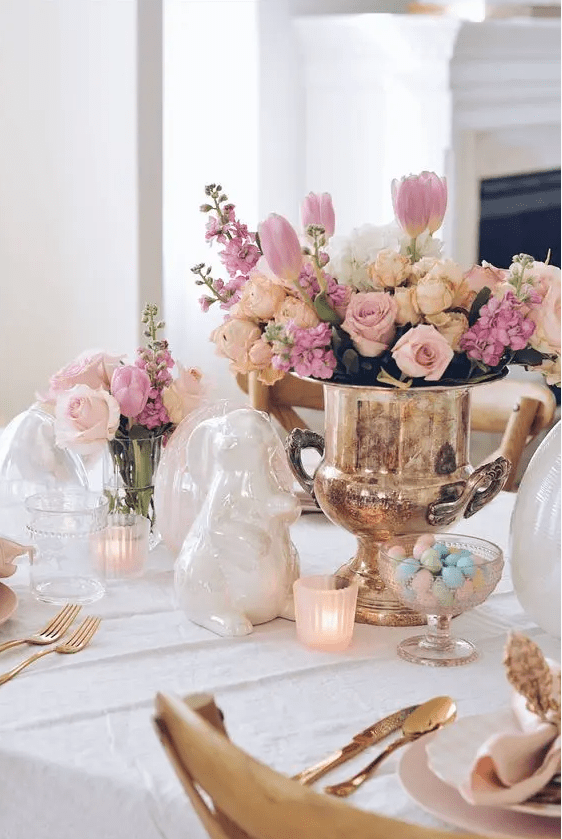an elegant and chic Easter table setting with a lovely floral centerpiece, candles, porcelain bunnies, gold cutlery and pastel candies