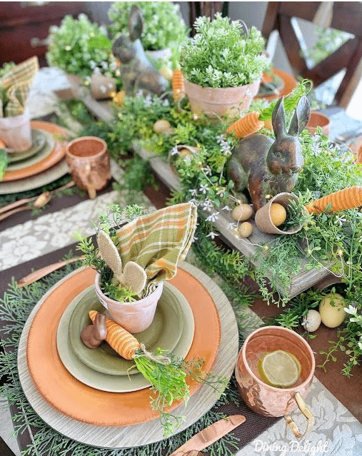 an organic Easter tablescape with lots of greenery, blooms, lights, bunny figurines and carrots and copper mugs