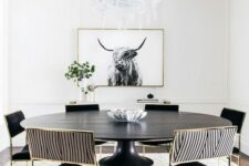 a bold and catchy black and white dining room with a round table, black and striped chairs, an artwork, a printed rug and greenery