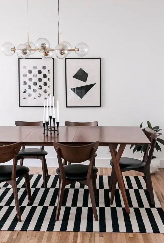 A bold black and white mid century modern dining space with a stained table and black chairs, a striped rug and a gallery wall
