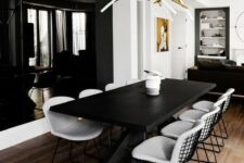 a bold dining room with a black accent wall, a black table and white chairs, a bold and catchy chandelier