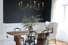a catchy dining room with black walls and white panels, a stained table, white armchairs and black chairs, a vintage chandelier