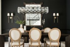 a chic and catchy black and white dining room with black walls, a dark-stained dining table, neutral chairs and a beautiful chandelier