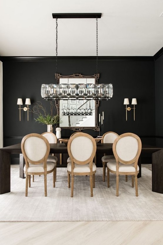 A chic and catchy black and white dining room with black walls, a dark stained dining table, neutral chairs and a beautiful chandelier