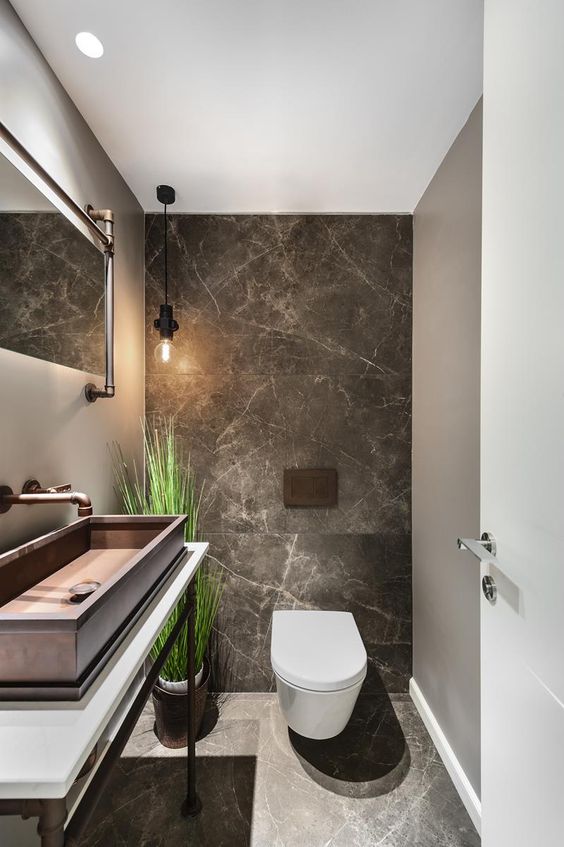 a chic guest toilet with stone tiles, a large metal sink, a fake potted plant and some pipes for an industrial feel