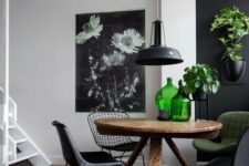 a contrasting black and white dining space with a black accent wall, a stained table, black and a green chair, greenery and green bottles