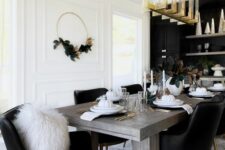 a glam dining room with a black accent wall and built-in cabinets, a stained table and black chairs, a gold chandelier