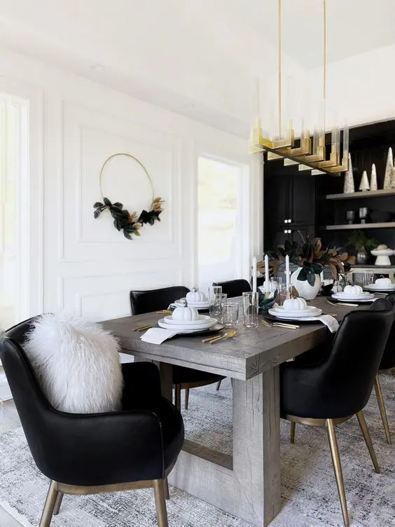 A glam dining room with a black accent wall and built in cabinets, a stained table and black chairs, a gold chandelier