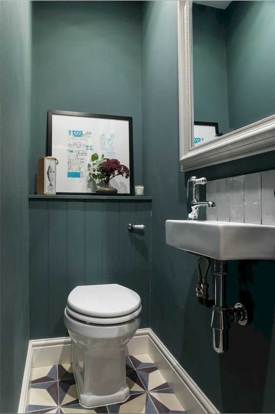 A guest toilet done with teal walls, a large mirror in a frame, some artworks and a wall mounted sink