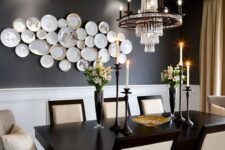 a jaw-dropping dining room with black walls, a black table, neutral chairs, a chic chandelier and a gallery wall of plates