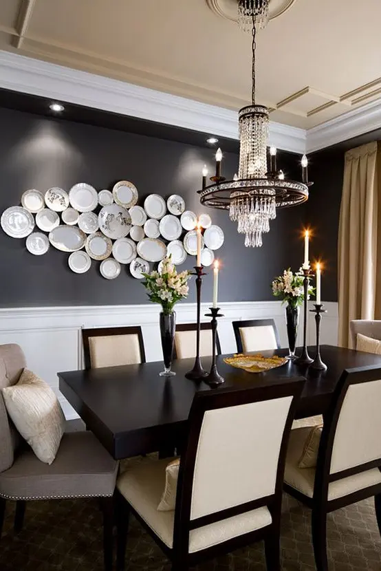 A jaw dropping dining room with black walls, a black table, neutral chairs, a chic chandelier and a gallery wall of plates