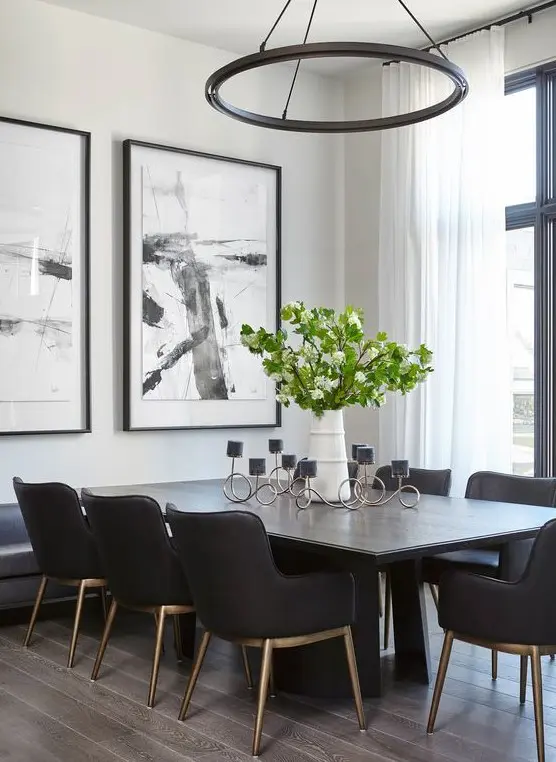 A light filled black and white dining room with white walls, a black table and chairs, a round chandelier and catchy artwork