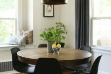 a mid-century modern dining nook with a round table, black chairs, a black pendant lamp, greenery and printed pillows