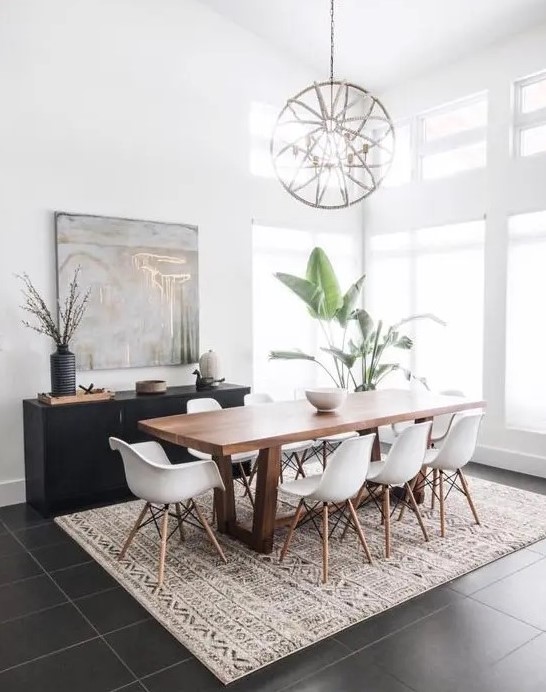 A mid century modern dining space with a stained table and white Eames chairs, a printed rug, a black credenza, a sphere chandelier and potted plants