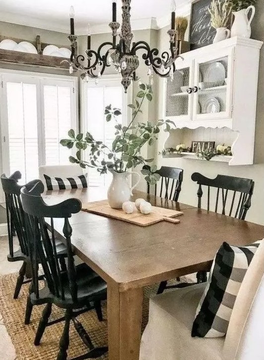 A modern farmhouse dining space done in black and white, with a stained table,a white wall mounted shelf and black chairs, a vintage chandelier