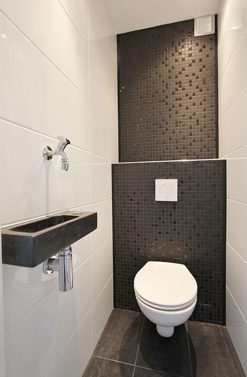 A monochromatic guest toilet with black and white tiles of different scales and a wall mounted stone sink