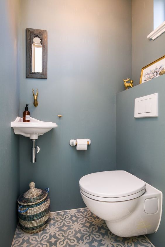 a small and simple guest toilet with a tiny wall-mounted sink, a small mirror, a basket for storage and a toilet