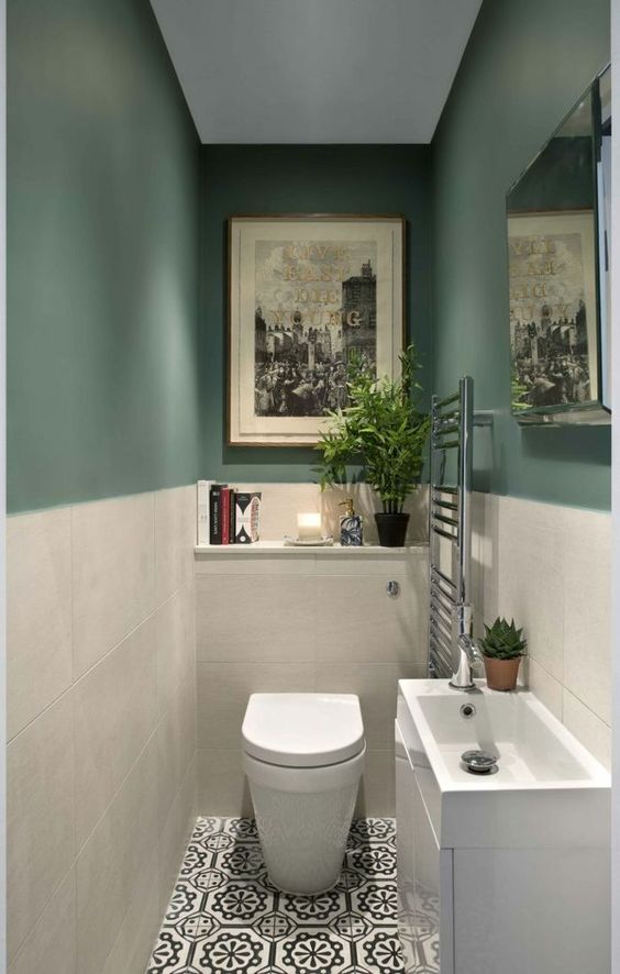 a small and stylish guest toilet with green and white tile walls, a sink with a vanity for storage and some artworks