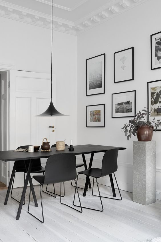 a stylish black and white dining space with a black table and chairs, a catchy pendant lamp, a free form gallery wall and a potted plant