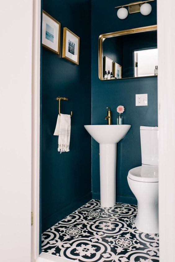 a stylish guest toilet with navy walls, brass fixtures, a mirror and artworks plus a wall lamp
