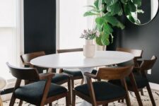 a stylish mid-century modern dining room with black walls and white window frames, an oval table and black chairs, a round mirror and a gilded chandelier