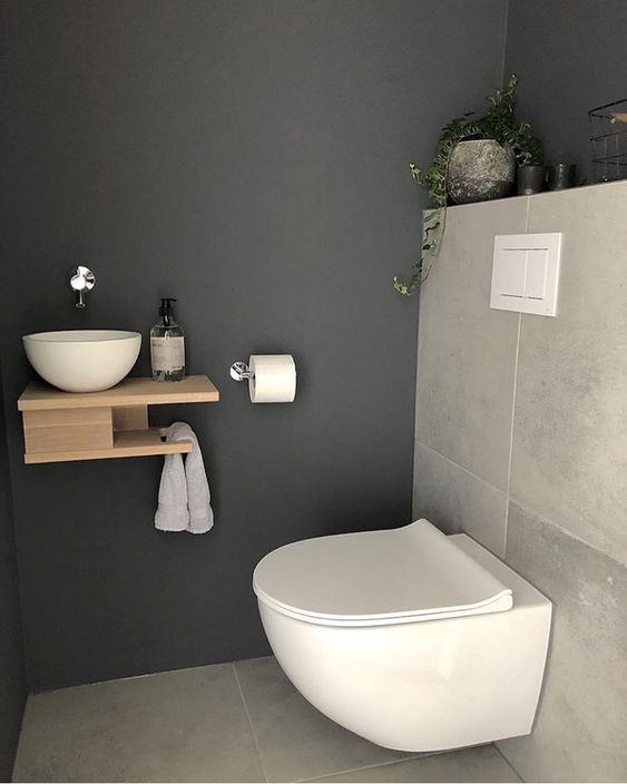 A tiny guest toilet with stone tiles, a wall mounted wooden vanity with a vessel sink and a potted plant