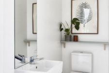 an all-white guest toilet with a wall-mounted sink, a tall mirror, a plant and a tropical artwork