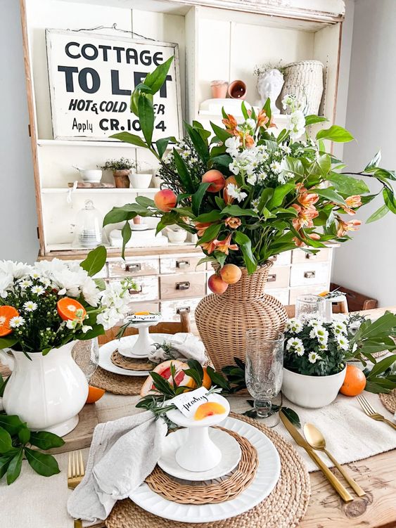 a bright Mother's Day table setting with wicker placemats, a wicker vase with blooms and fruit, white flowers and gold cutlery