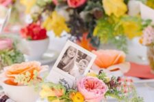 a bright Mother’s Day tablescape with bold blooms and greenery, coral napkins and photos plus silver cutlery