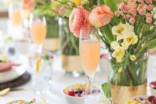 a bright Mother’s Day tablescape with yellow and pink blooms, greenery and twigs, wicker placemats, pink napkins and gold cutlery