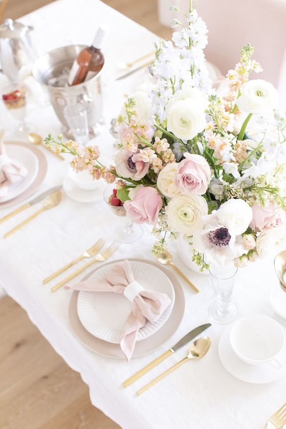 a delicate Mother's Day table setting with pastel and neutral blooms, grey and white plates and blush napkins