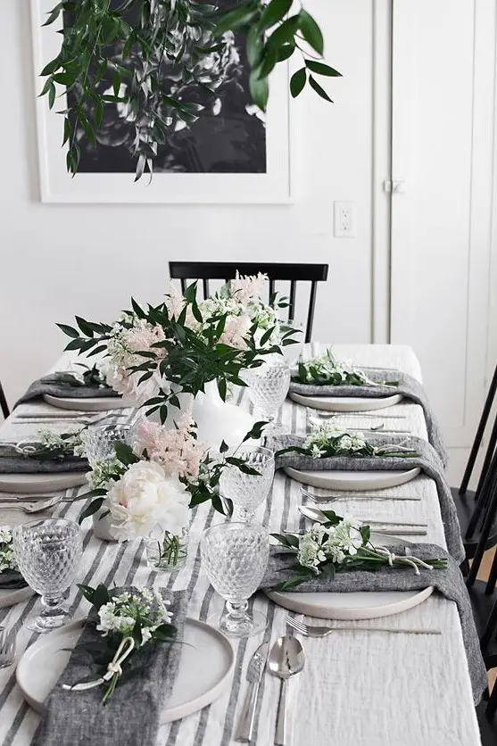 a modern spring tablescape with white and blush blooms and greenery, grey napkins, a striped runner and cool glasses