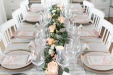 a pretty Mother’s Day table setting with a printedrunner and napkins, a greenery and blush bloom runner, candles and gold cutlery