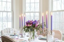 a refined colorful spring tablescape with a bright floral centerpiece, purple candles, printed plates and chargers