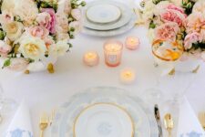a sophisticated pastel Mother’s Day table setting with pink and blush blooms, pink candles, blue plates and gold cutlery