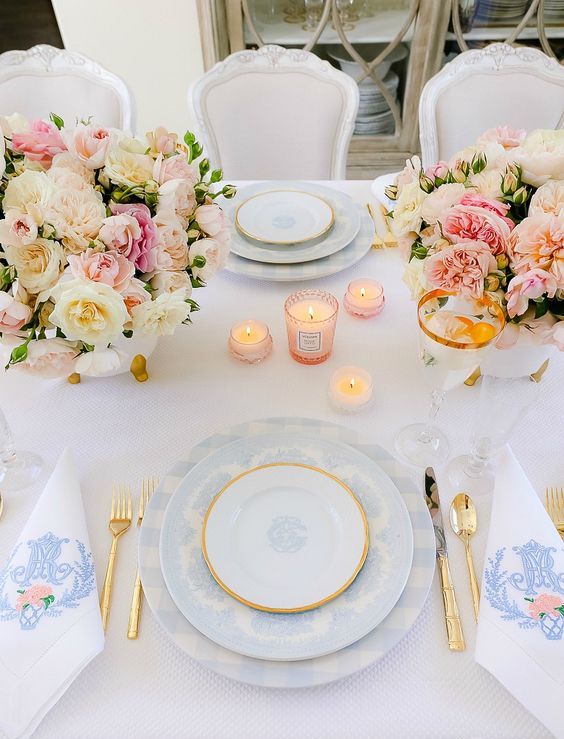 a sophisticated pastel Mother's Day table setting with pink and blush blooms, pink candles, blue plates and gold cutlery