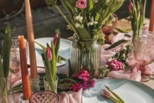 a sophisticated pink Mother’s Day tablescape with a pink runner, pink blooms and glasses, ornage candles and wicker placemats