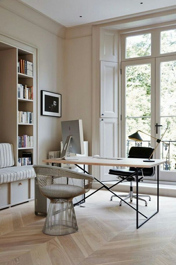 A beautiful neutral home office with built in storage units and a daybed, a laconic desk, a black and a silver chair, an entrance to a balcony