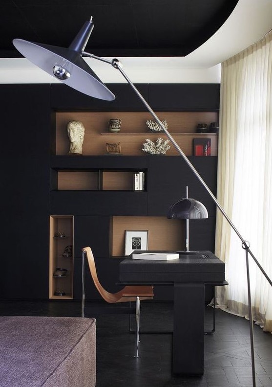 A mid century modern home office with a black wall, a rich stained niches, a black desk and stylish lamps