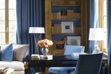 a refined blue home office with a chic black desk, blue chairs, walls and textiles and elegant touches of gold here and there