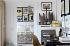 a sophisticated home office with a refined black desk, a neutral chair, a gallery wall, a bit of artworks and a crystal chandelier