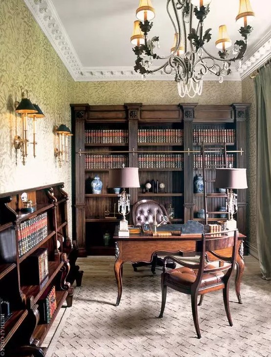 A vintage home office with dark stained bookcases and bookshelves, a dark stained desk and leather chairs, table and wall lamps and a cool chandelier
