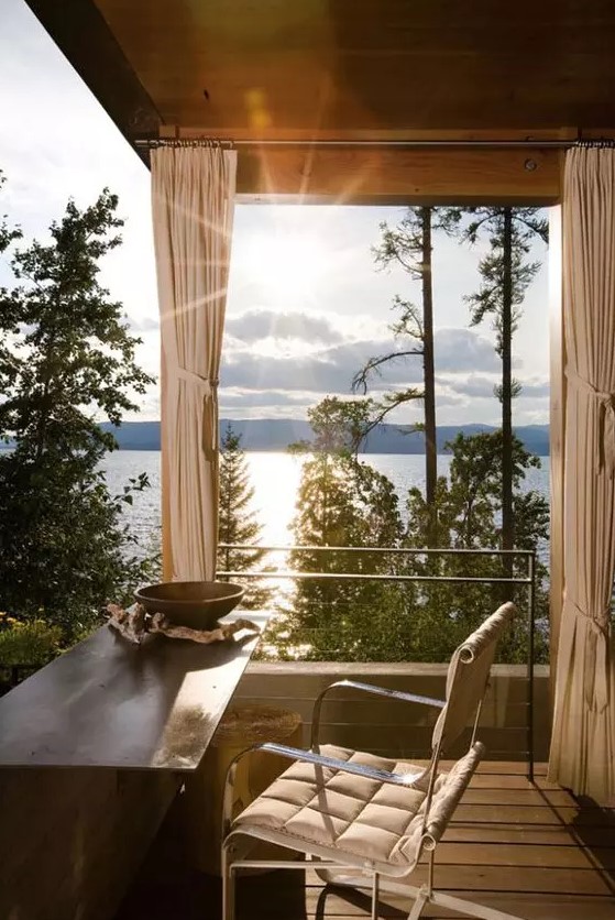 An adorable home office with glazed walls, jaw dropping views of the lake, a metal desk and a comfy chair is a lovely space to enjoy the views and get inspired