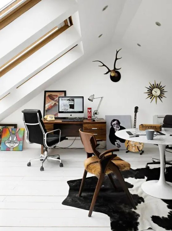 an eclectic attic home office with large skylights, a stained desk and a black leather chair, a round table and a wooden chair, a cool rug and some artworks