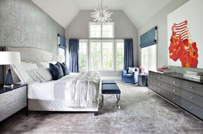 a luxurious grey bedroom dotted with navy blue accents - stools, curtains, Roman shades and pillows