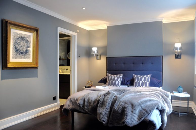 a contemporary bedroom with grey walls and furniture and a stunning upholstered navy bed plus grey pillows and a blanket