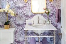 a beautiful purple and white bathroom with printed wallpaper, gilded touches and lamps and an orchid