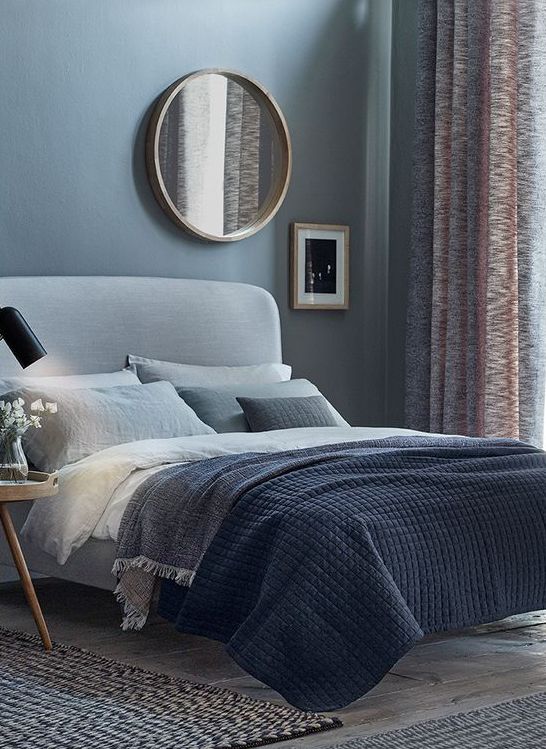 a blue bedroom with light grey floors and a light grey upholstered bed plus grey bedding