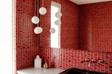 a bright red bathroom clad with bold mosaic tiles, a dark sink and pendant lamps